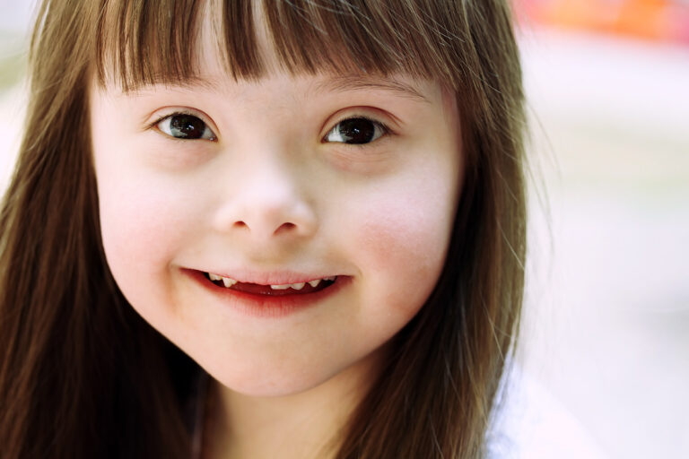 Smiling young girl with Down syndrome and long brown hair looking at the camera