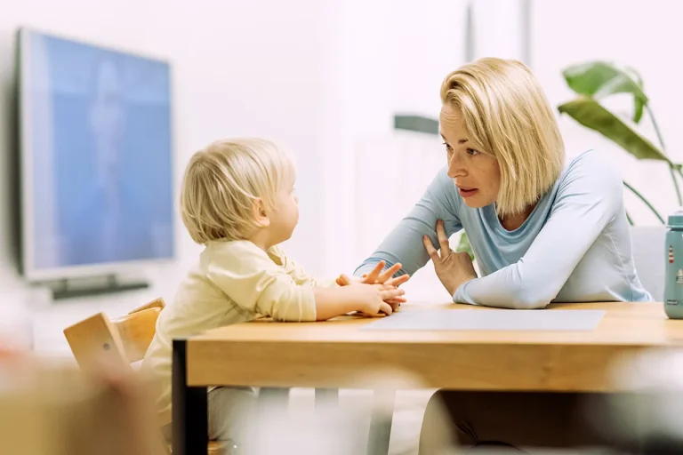 A mother practices speech sounds face to face with her toddler at the table