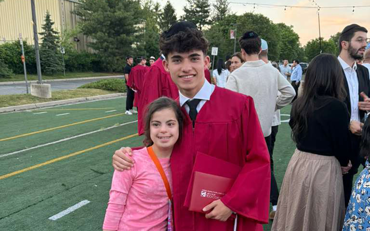 Eytan Rosilio in his red graduation gown with his arm around his younger sister Liran, who is smiling in a pink outfit