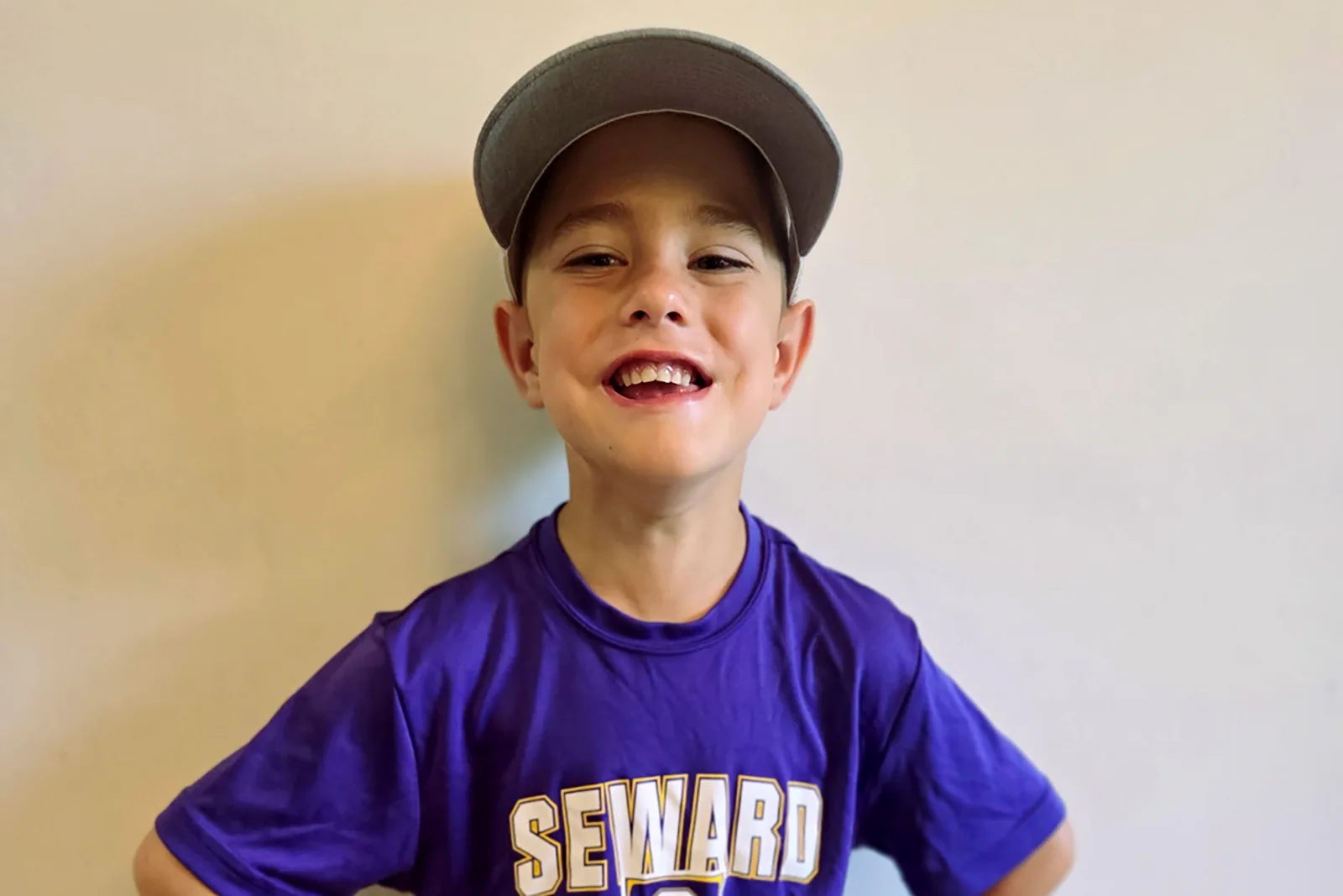 Milo, smiling in a ball cap and purple Seward t-shirt
