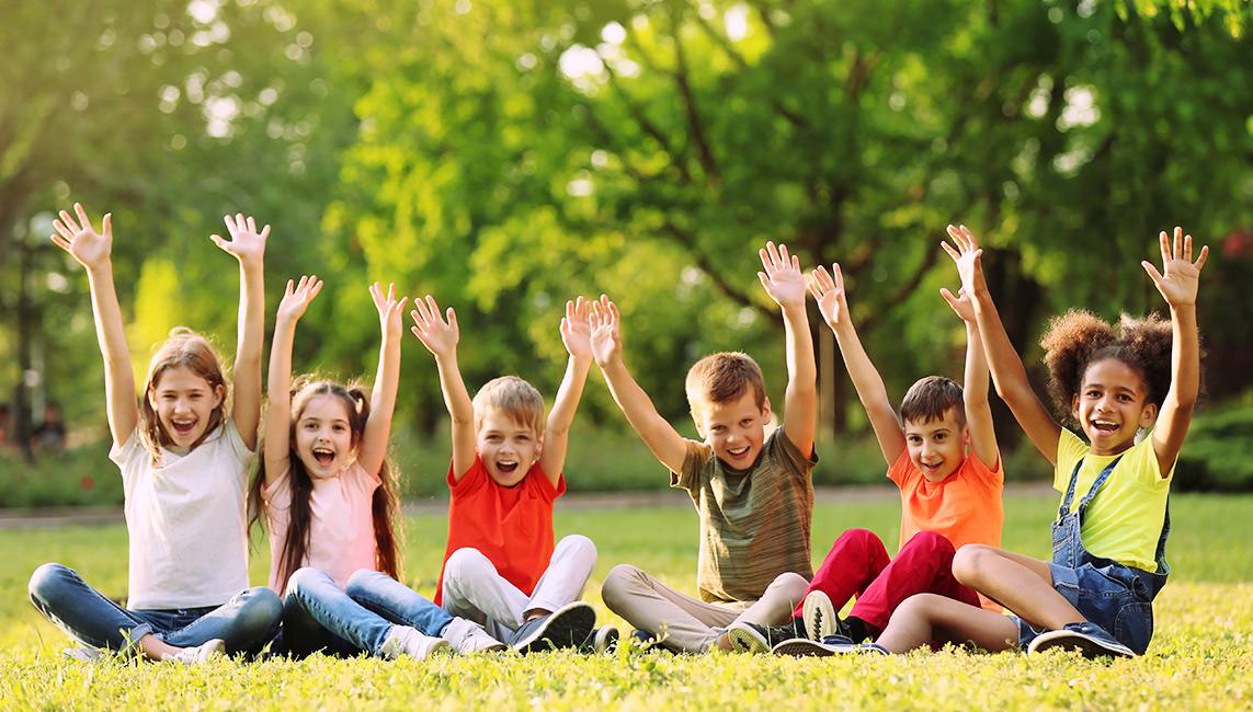 Children sitting together outdoors with their hands raised