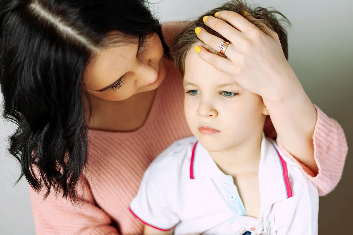 A mother holds her hand to her young son's forehead, checking on him with concern